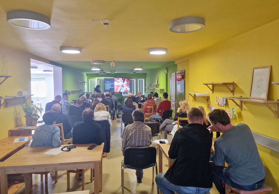 Udeleženci sedijo na stolih v dvorani slika od zadaj